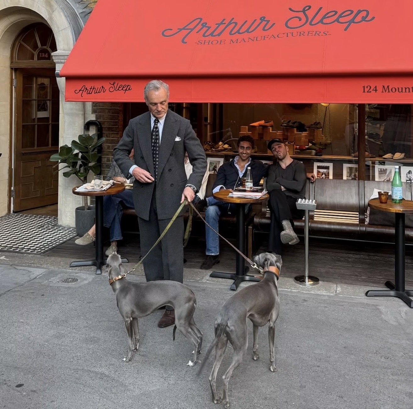 A man in a double-breasted suit with two grey whippets outside Arthur Sleep, 124 Mount Street